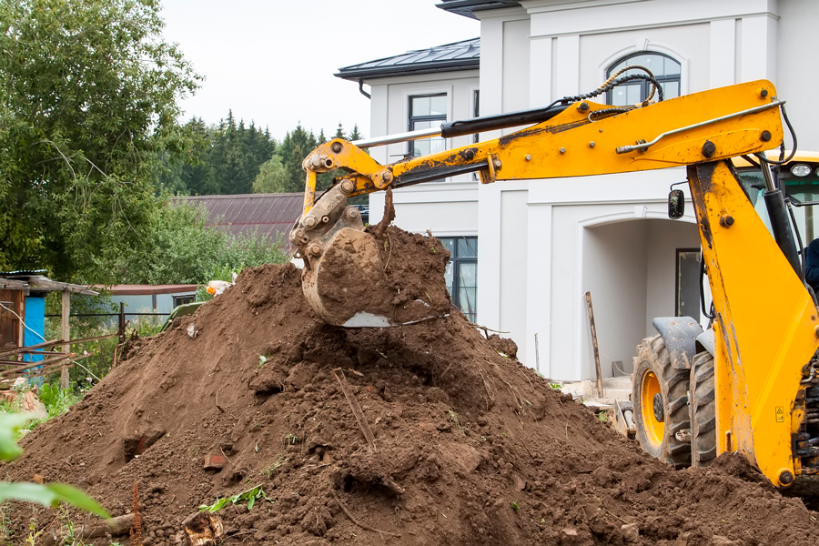 Yellow bucket excavator levels pile of earth in front of country cottage 